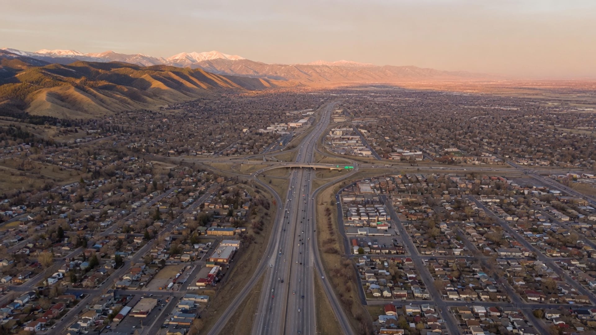 Aerial view of the Denver metro freeway network at golden hour showing east-metro Aurora through downtown Denver to foothills Evergreen